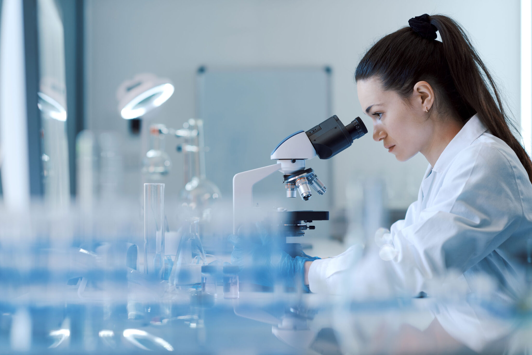 A female lab worker operating a microscope.