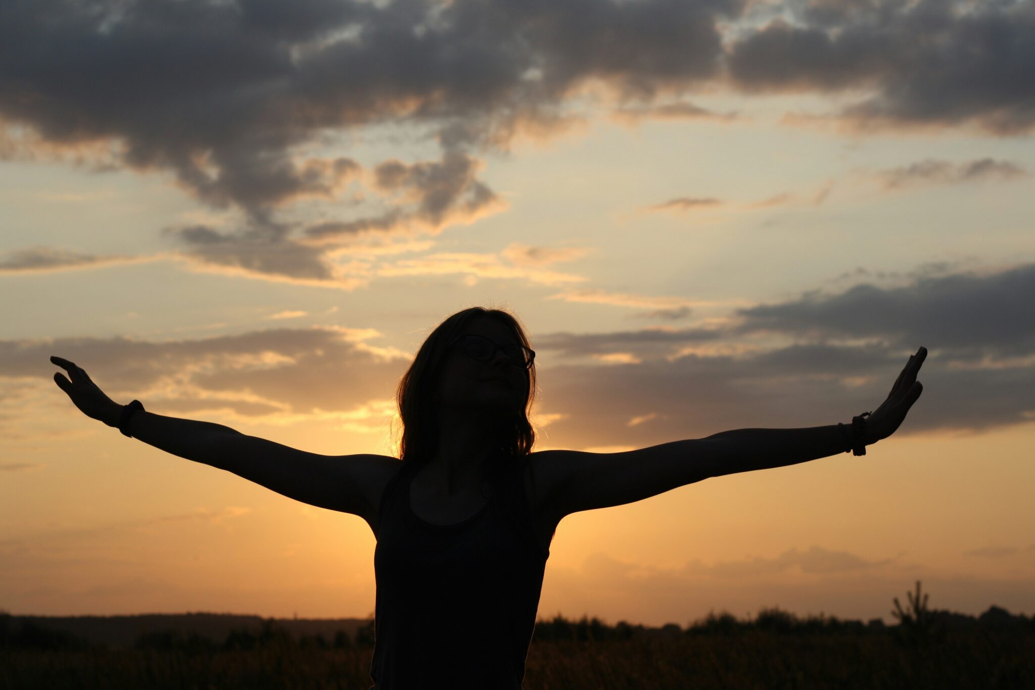 A woman facing the sunset, arms stretched out to the side of her body.